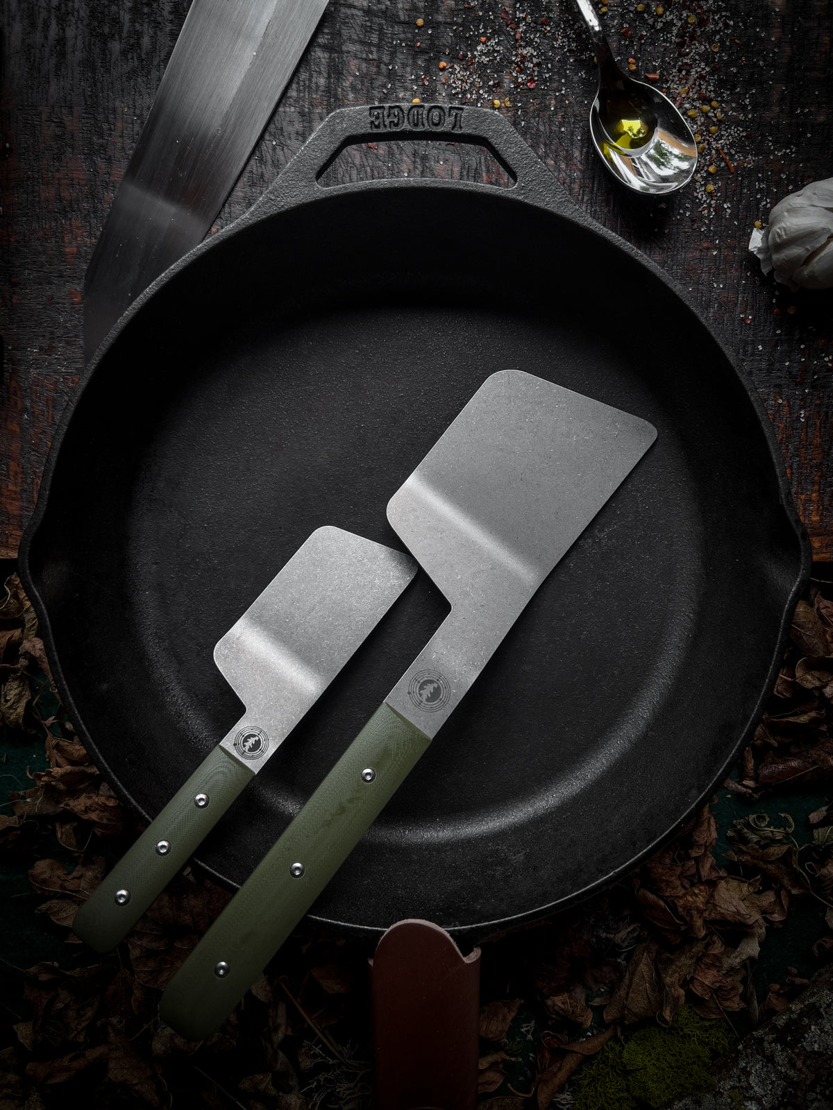 a full size and mini size green handle spatula sitting in a skillet